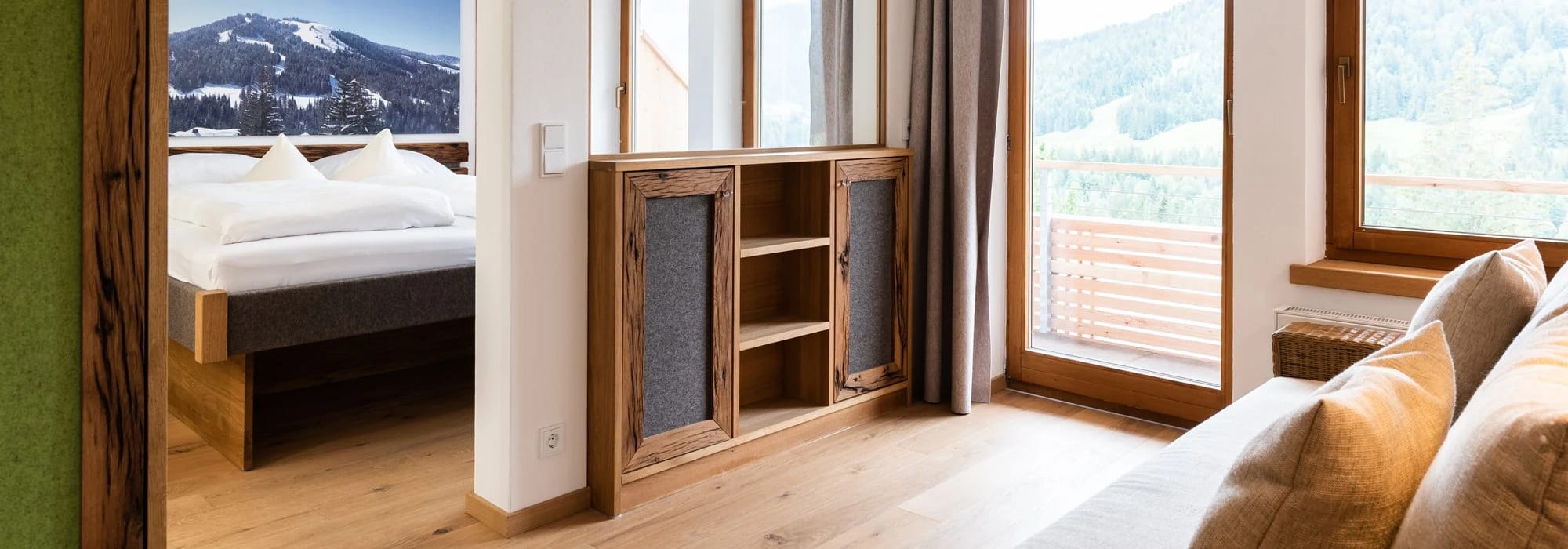 Hotelzimmer mit Holzmöbeln, Doppelbett und Bergblick durch den Balkon