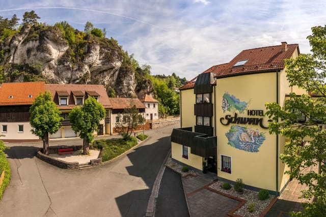 Außenansicht des Hotels Schwan mit gelber Fassade, Wandmalerei und Schriftzug vor bewaldeter Felswand