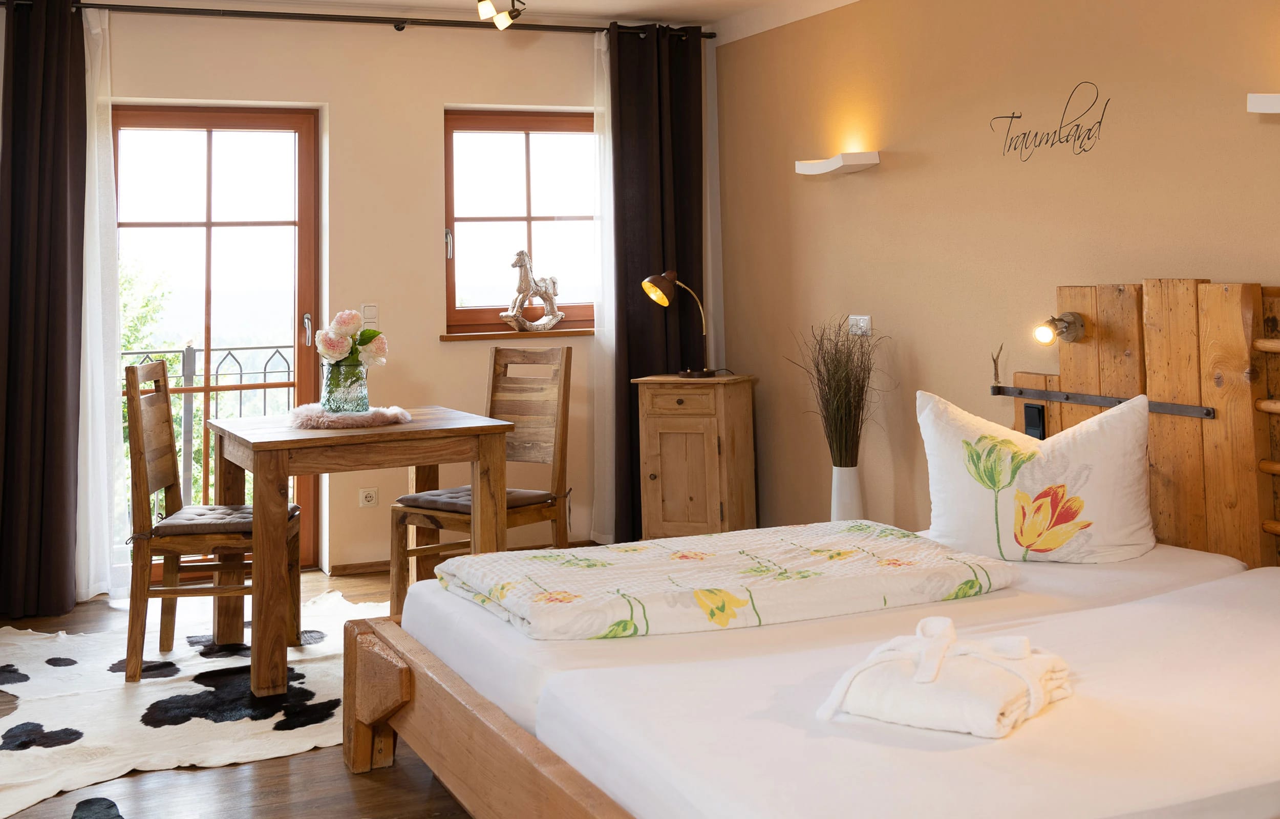 Zimmer mit Holzbett, Kuhfell-Teppich, Bauernmöbeln und Sitzplatz am Fenster