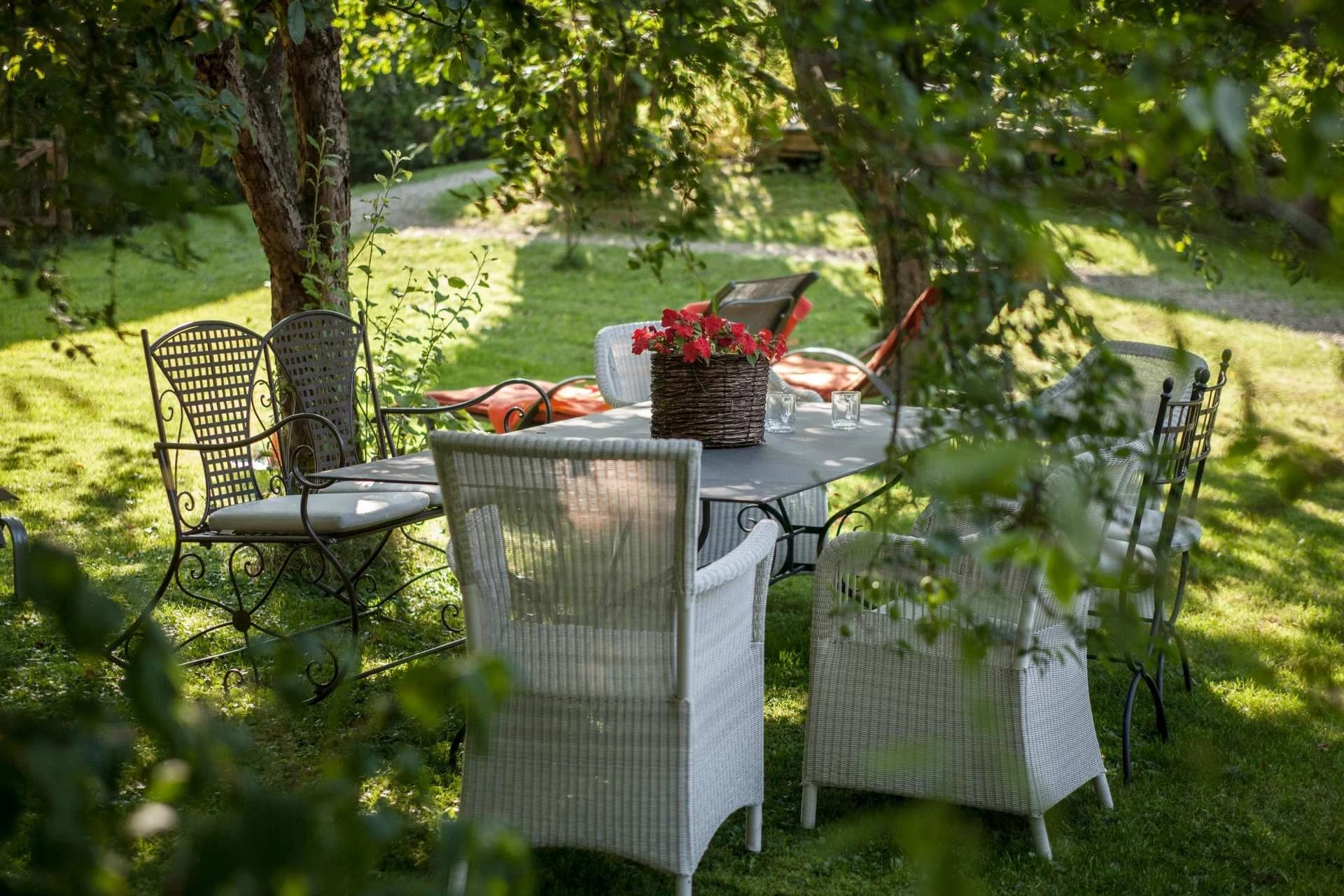Gedeckter Gartentisch mit weißen Korbsesseln im schattigen Grünen