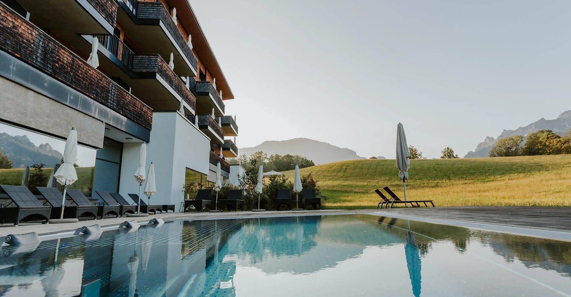 Außenpool des Klosterhof Hotels mit Sonnenliegen und Spiegelung der Berge im Wasser
