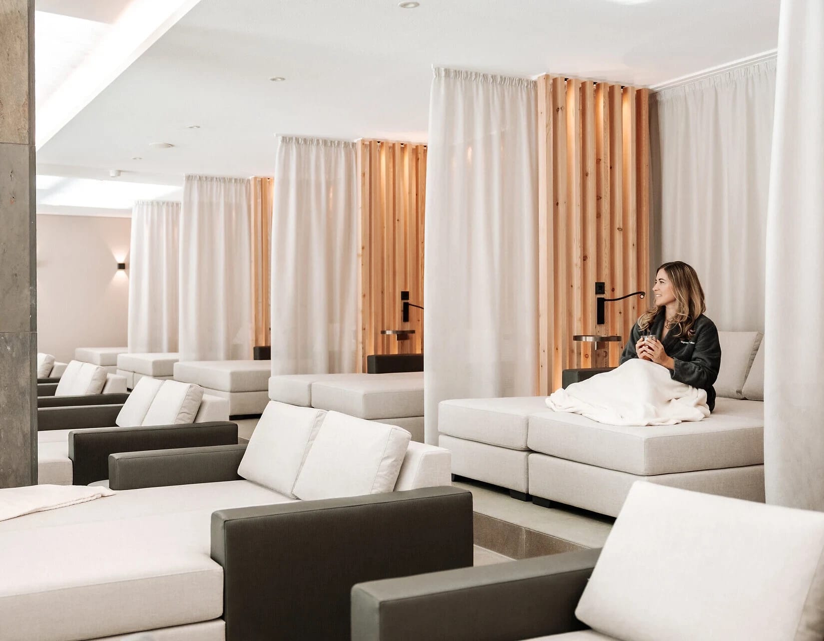 Spa-Ruheraum mit weißen Loungesofas und Holzlamellen-Trennwänden