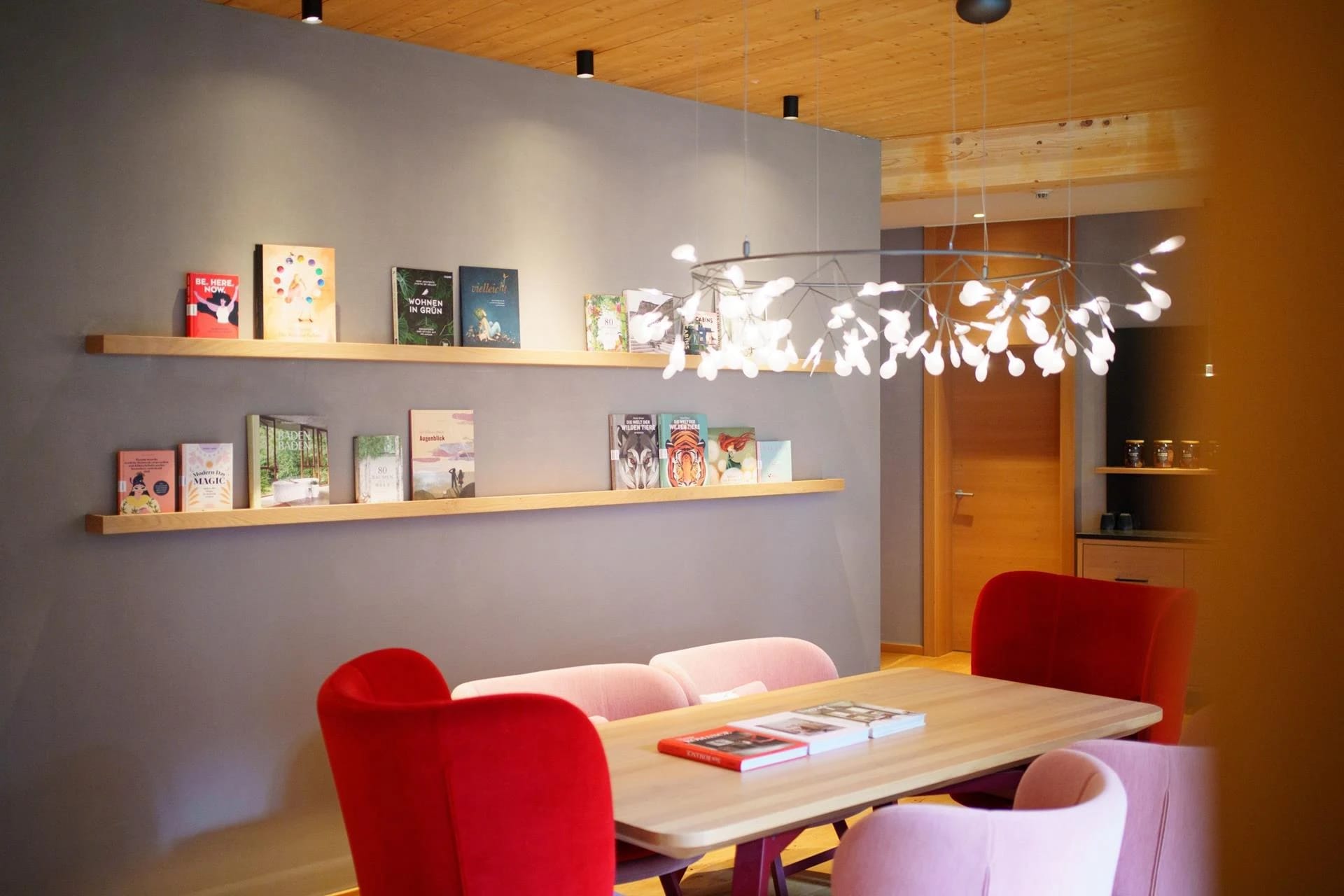 Lese-Lounge mit langem Tisch, roten und rosa Stühlen und Bücherregal
