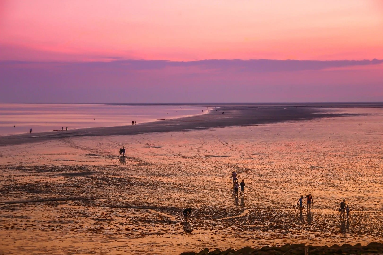 Spaziergänger im Watt bei rosa gefärbtem Abendhimmel
