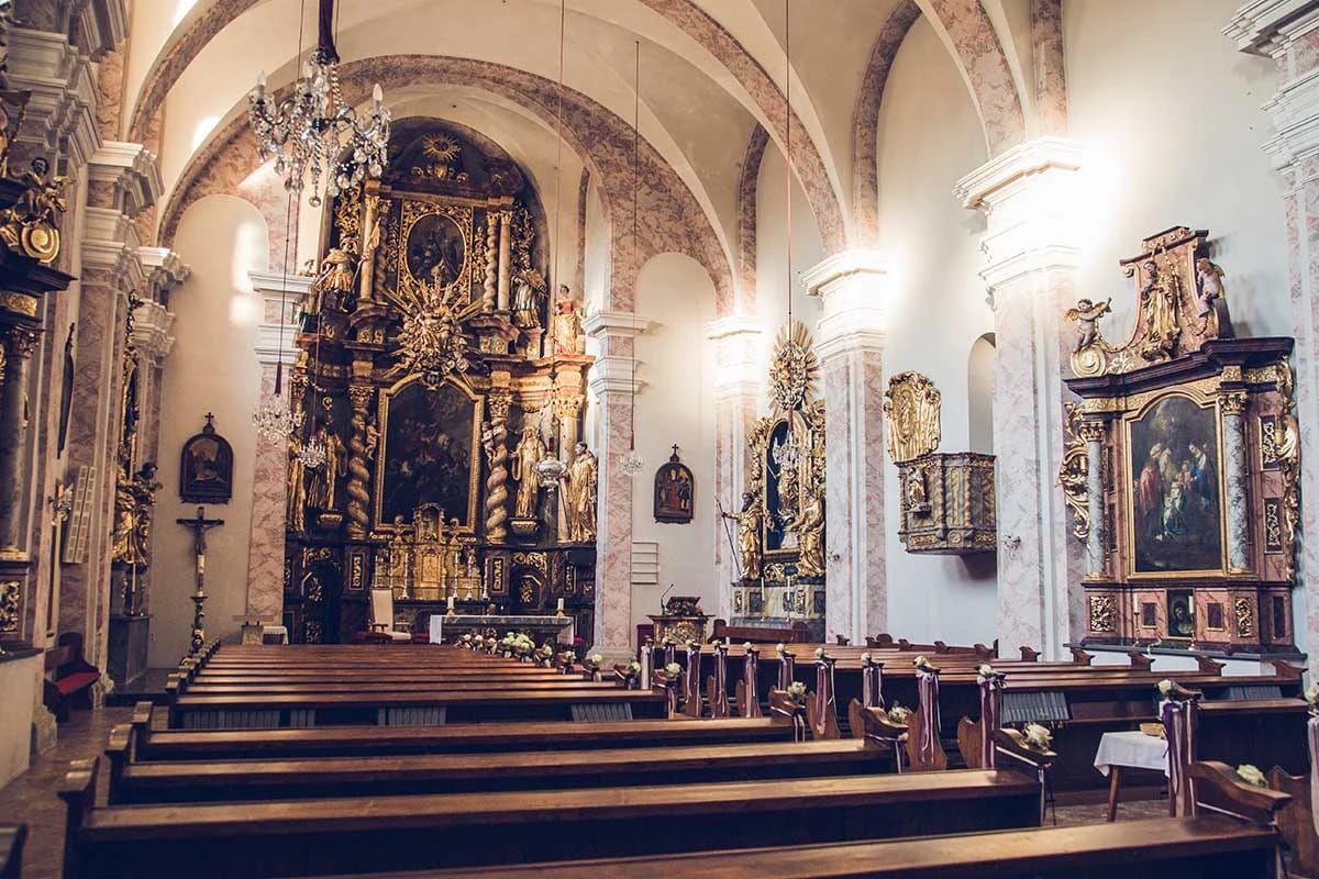 Barocker Innenraum der Stiftskirche mit vergoldetem Hochaltar, Seitenaltären und Holzbänken