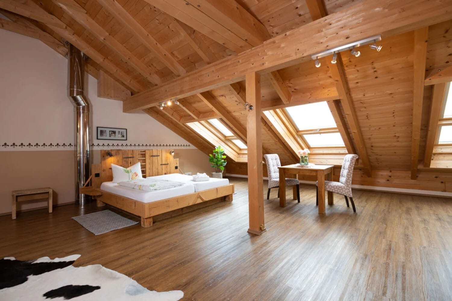 Dachgeschosszimmer mit offenem Holzdachstuhl, Doppelbett, Dachfenstern und Esstisch mit zwei Stühlen