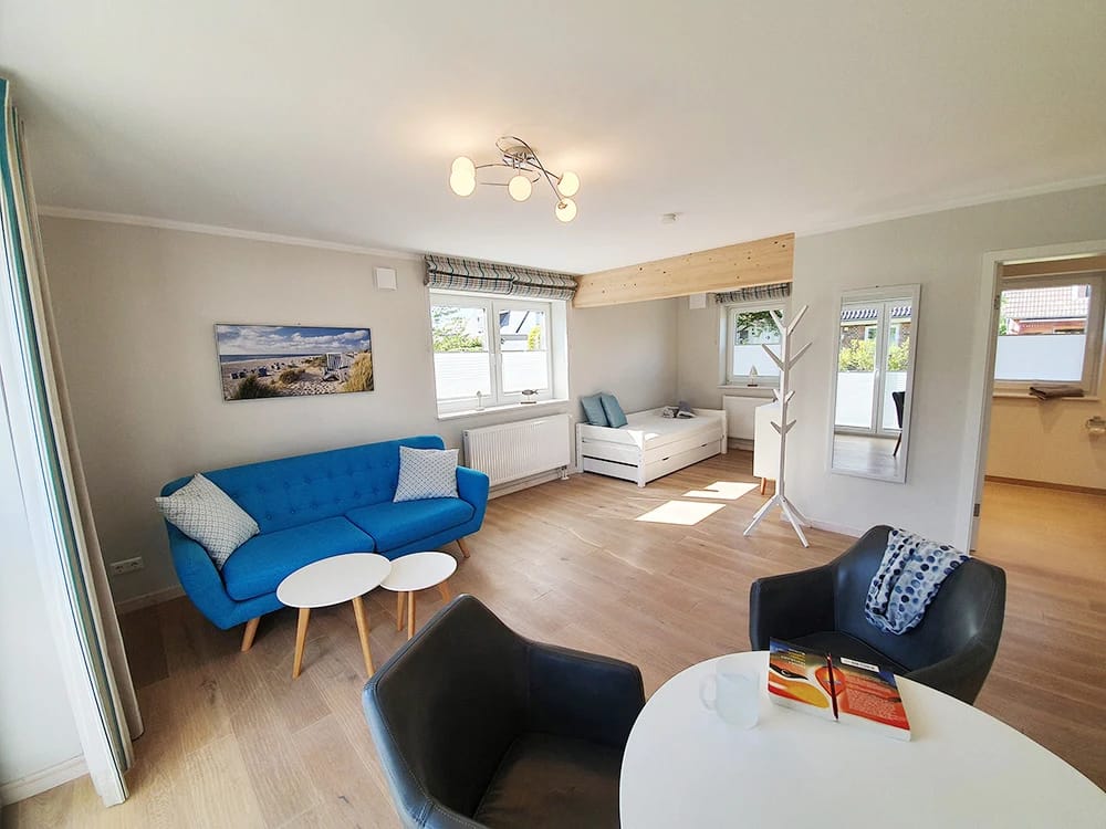 Wohnbereich mit blauem Sofa, zwei Sesseln und Couchtischen, im Nebenraum ein Bett