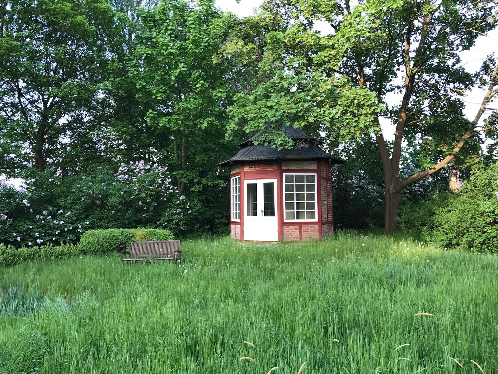 Kleines rotes Teehaus im hohen Gras am Rand des Parks