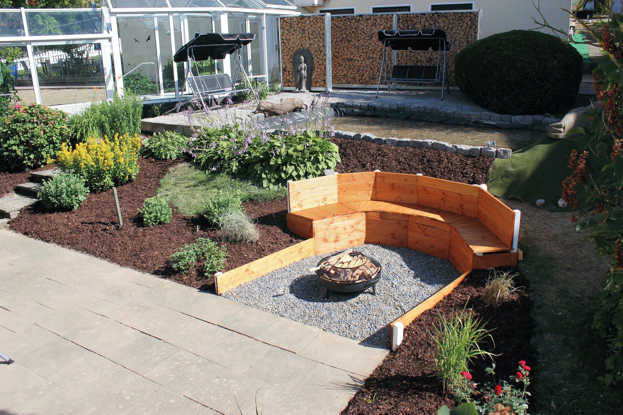 Hotelgarten mit Feuerschale, geschwungener Holzbank, Staudenbeeten und kleinem Teich