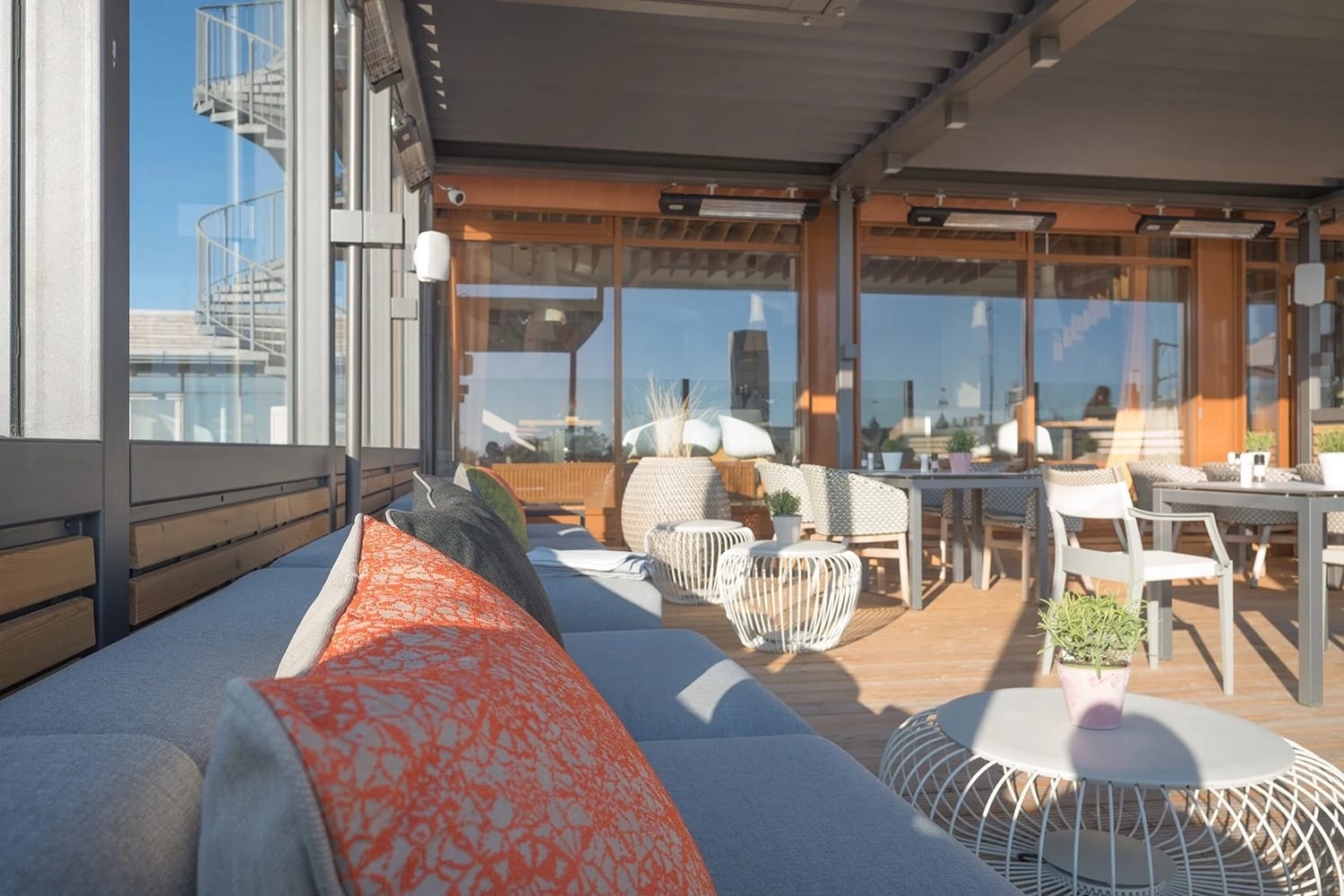 Überdachte Terrasse mit Loungesofa, Sesseln und Tischen hinter einer Glasfront