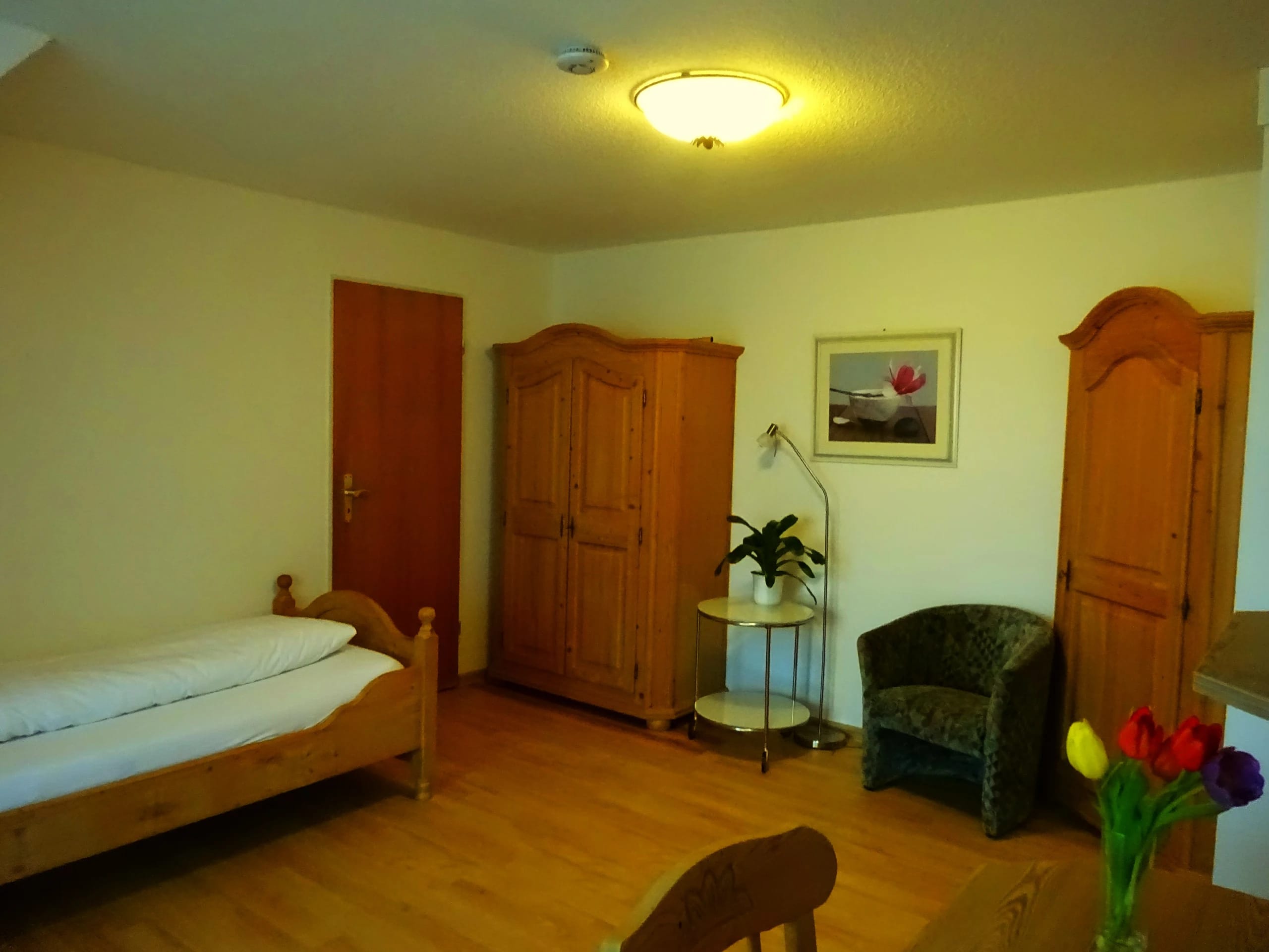 Zimmer mit Holzbett, zwei Bauernschränken aus Kiefernholz, Sessel und Beistelltisch mit Pflanze