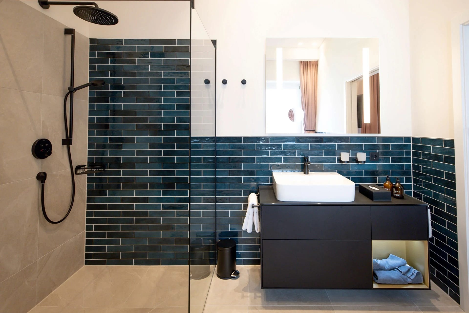 Badezimmer mit bodengleicher Dusche, dunkelgrün gefliester Wand und schwarzem Waschtisch