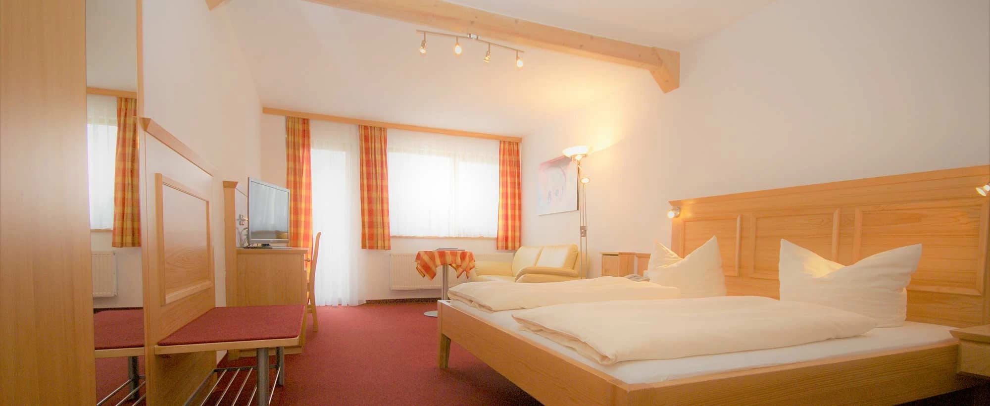 Gästezimmer mit Doppelbett, hellem Holzmobiliar, orange karierten Vorhängen und rotem Teppichboden