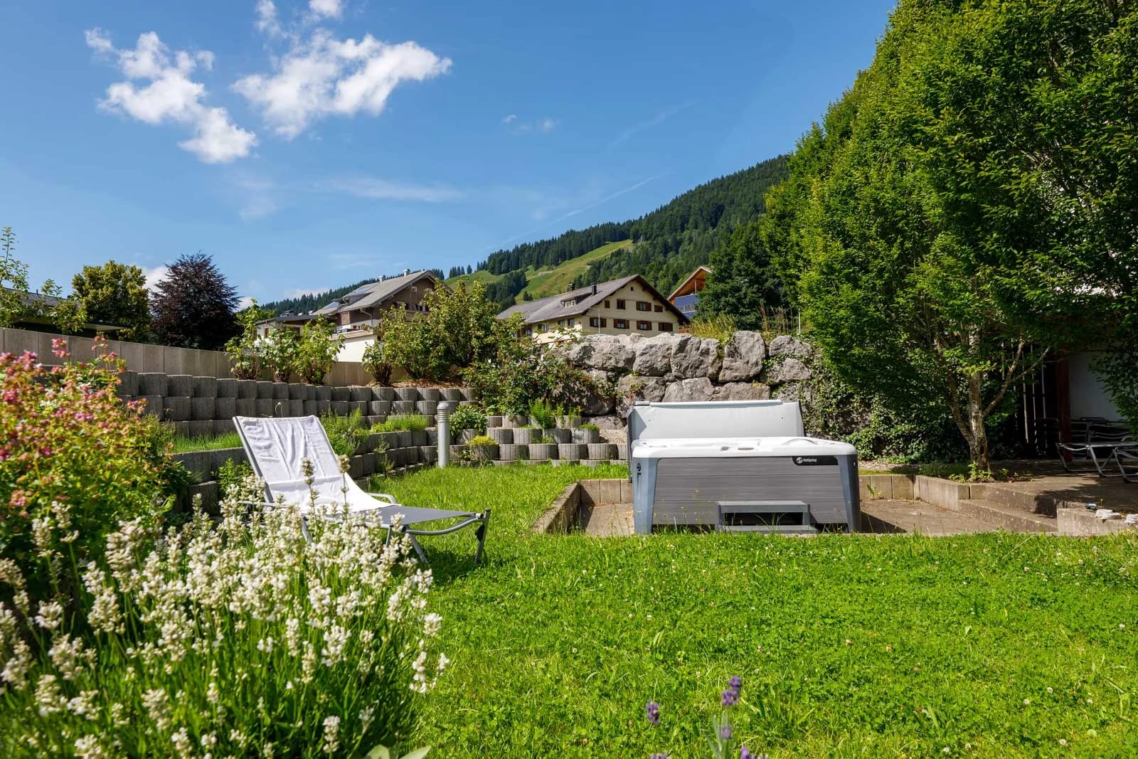 Whirlpool im grünen Garten mit Liege, Blumen und Blick auf die Berge