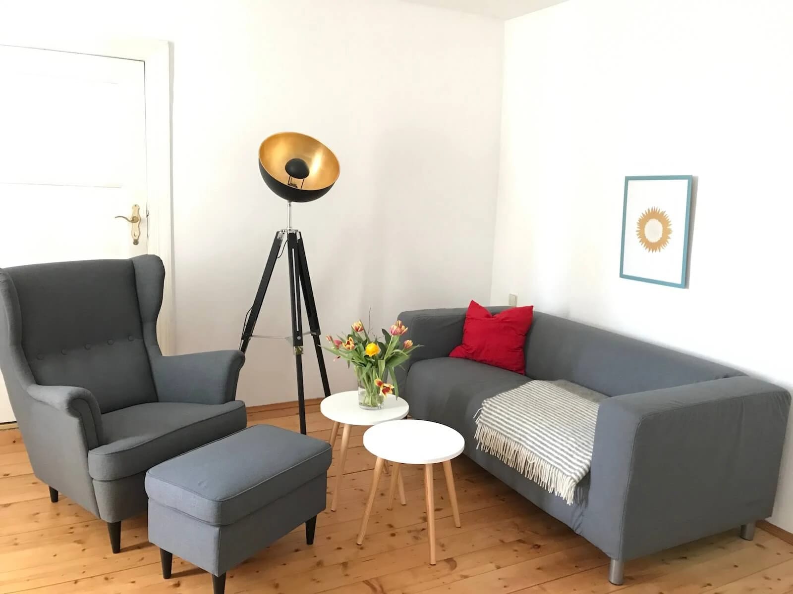 Wohnzimmer mit grauem Sofa, Sessel und Stehlampe auf hellem Dielenboden
