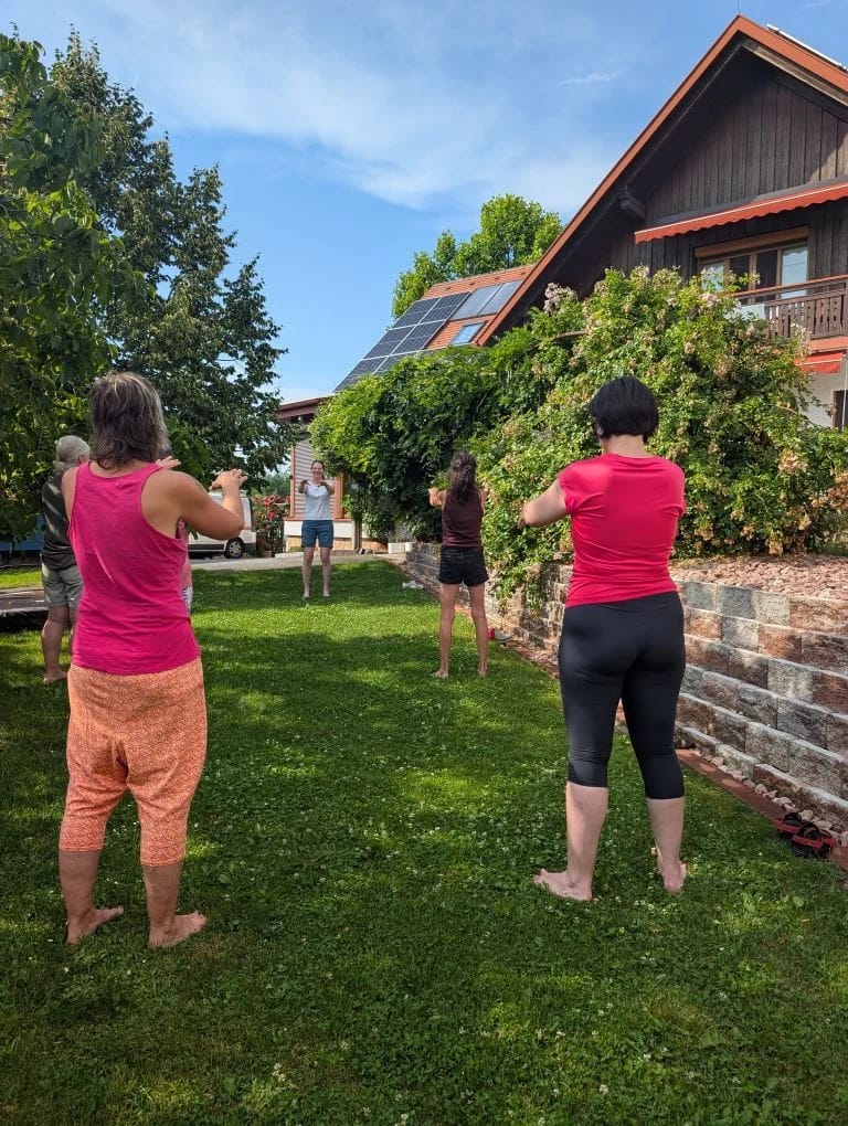 Vier Personen machen Qigong-Übungen auf einer Wiese vor einem Haus