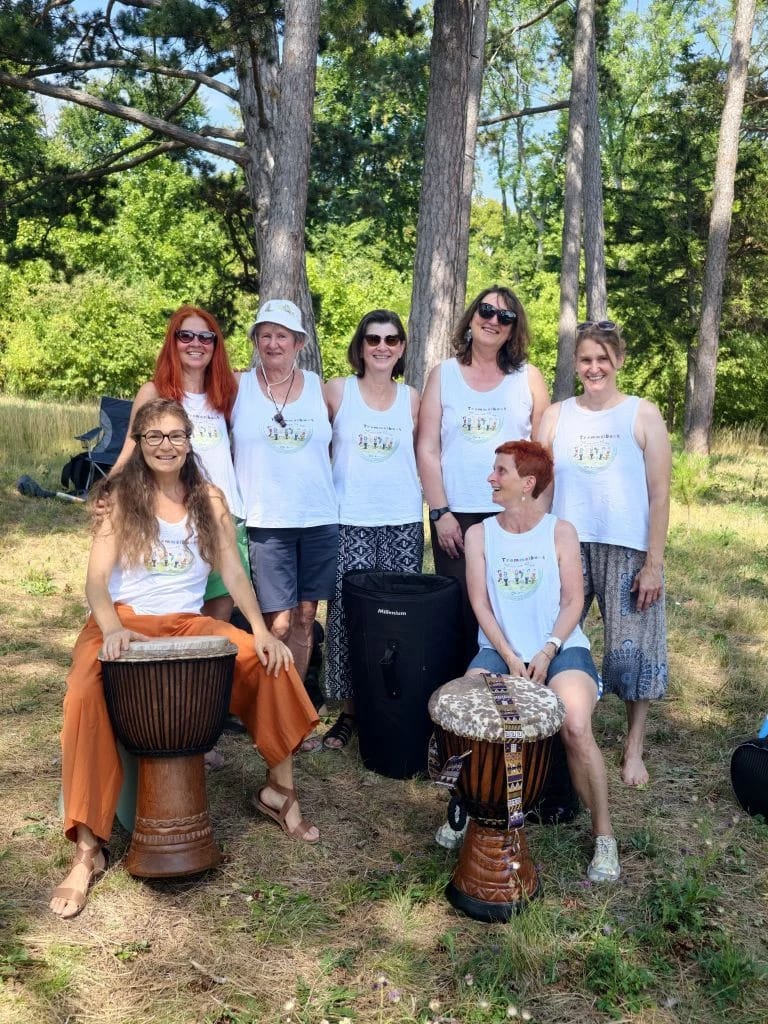 Sieben Frauen in gleichen T-Shirts posieren mit Trommeln im Wald