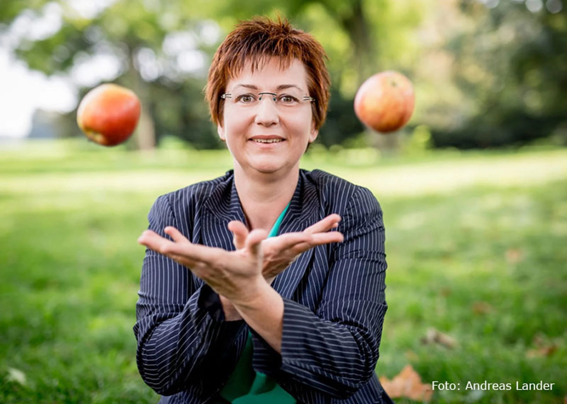 Porträt von Gabriele Brandes, lächelnd beim Jonglieren mit zwei Äpfeln im Park