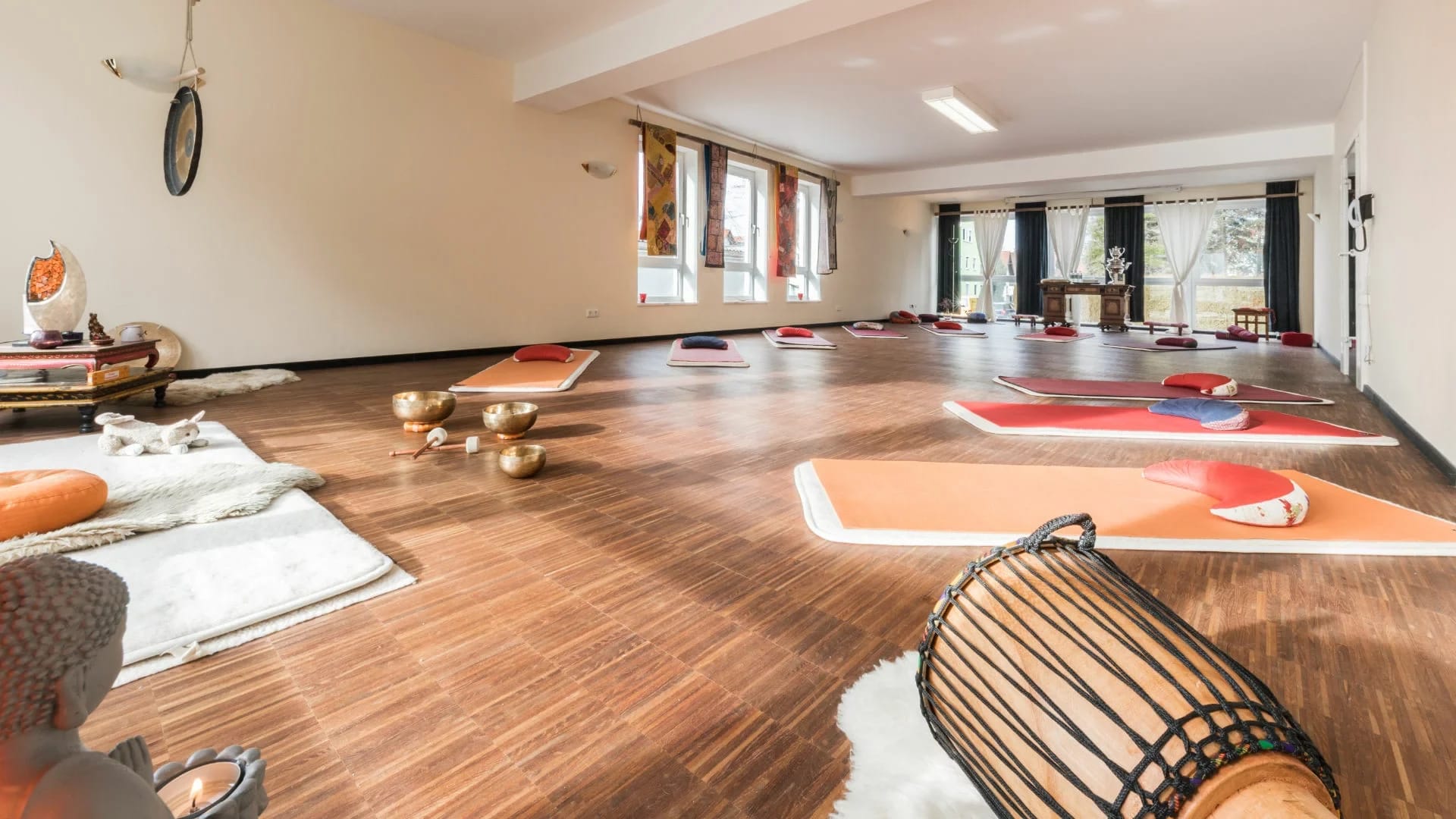 Yogaraum mit Holzboden, ausgelegten Matten, Kissen und Klangschalen