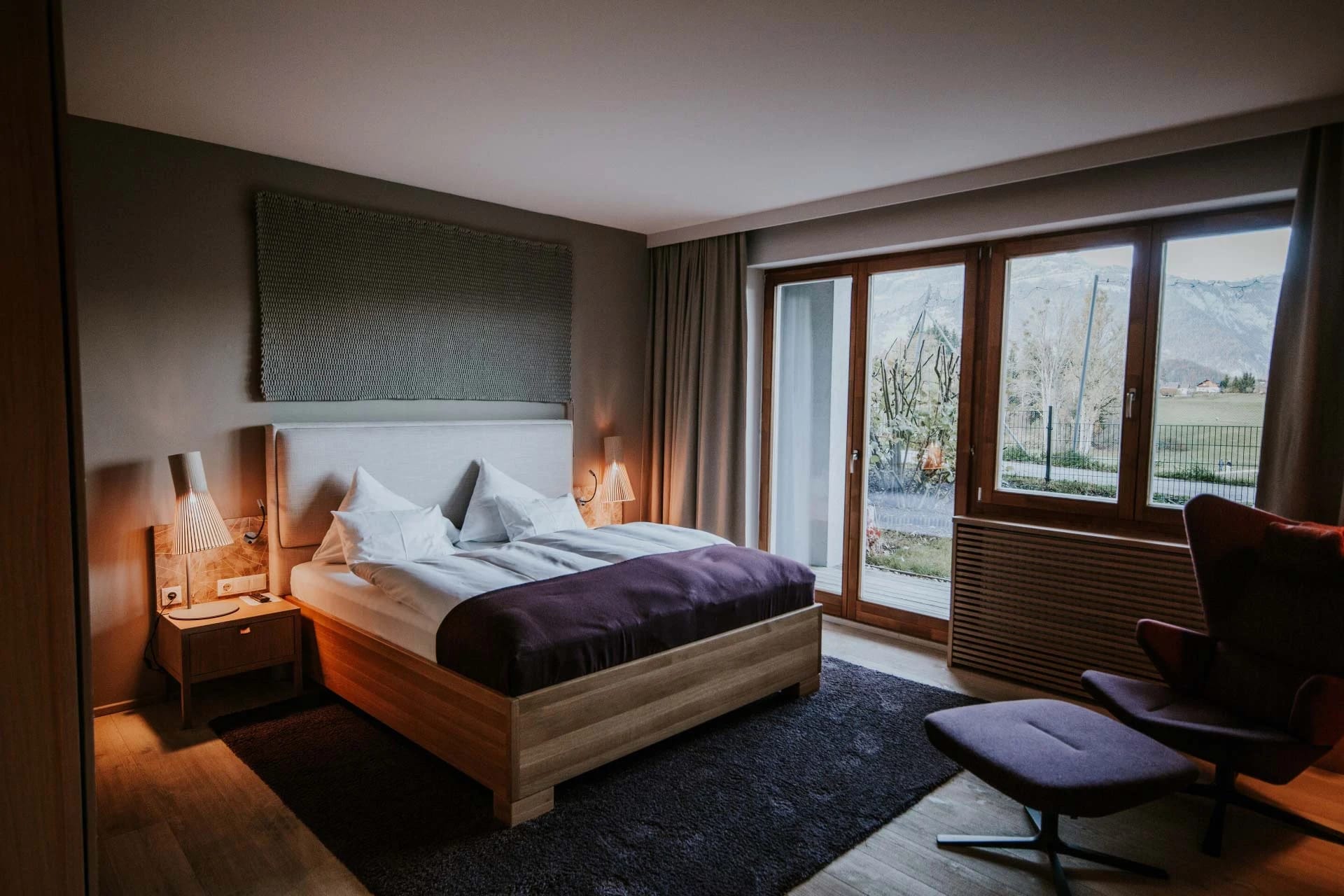 Schlafzimmer der WOW Suite mit großer Glasfront und Blick auf Wiese und Berge