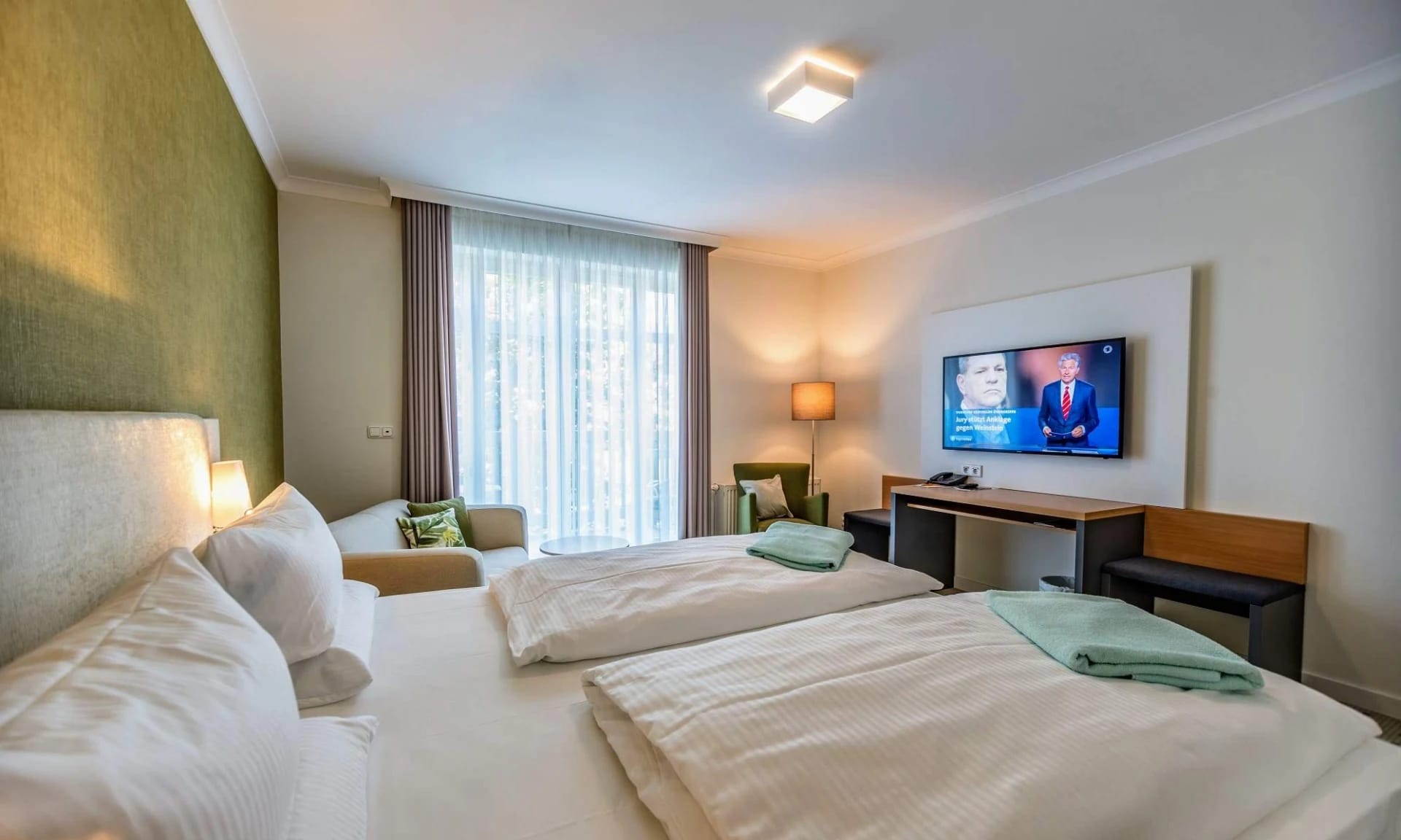 Doppelzimmer mit grüner Wandgestaltung, Sitzbereich und Flachbildfernseher