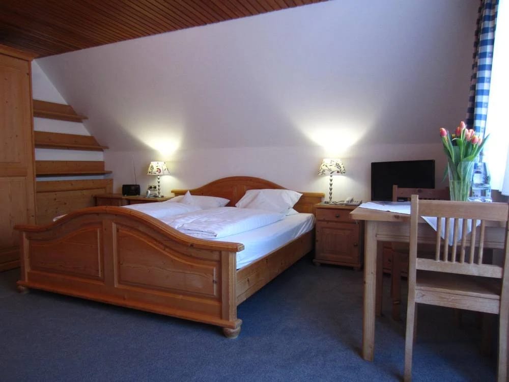 Doppelzimmer unter Dachschräge mit Holzbett, zwei Wandleuchten, Schreibtisch mit Stuhl und Fernseher
