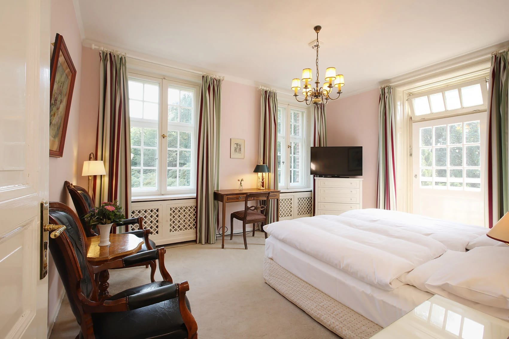 Zimmer in Rosétönen mit Doppelbett, Kronleuchter und Schreibtisch