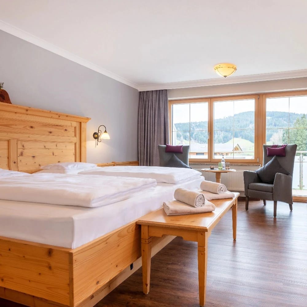 Doppelzimmer mit Holzbett, Sessel und großem Fenster