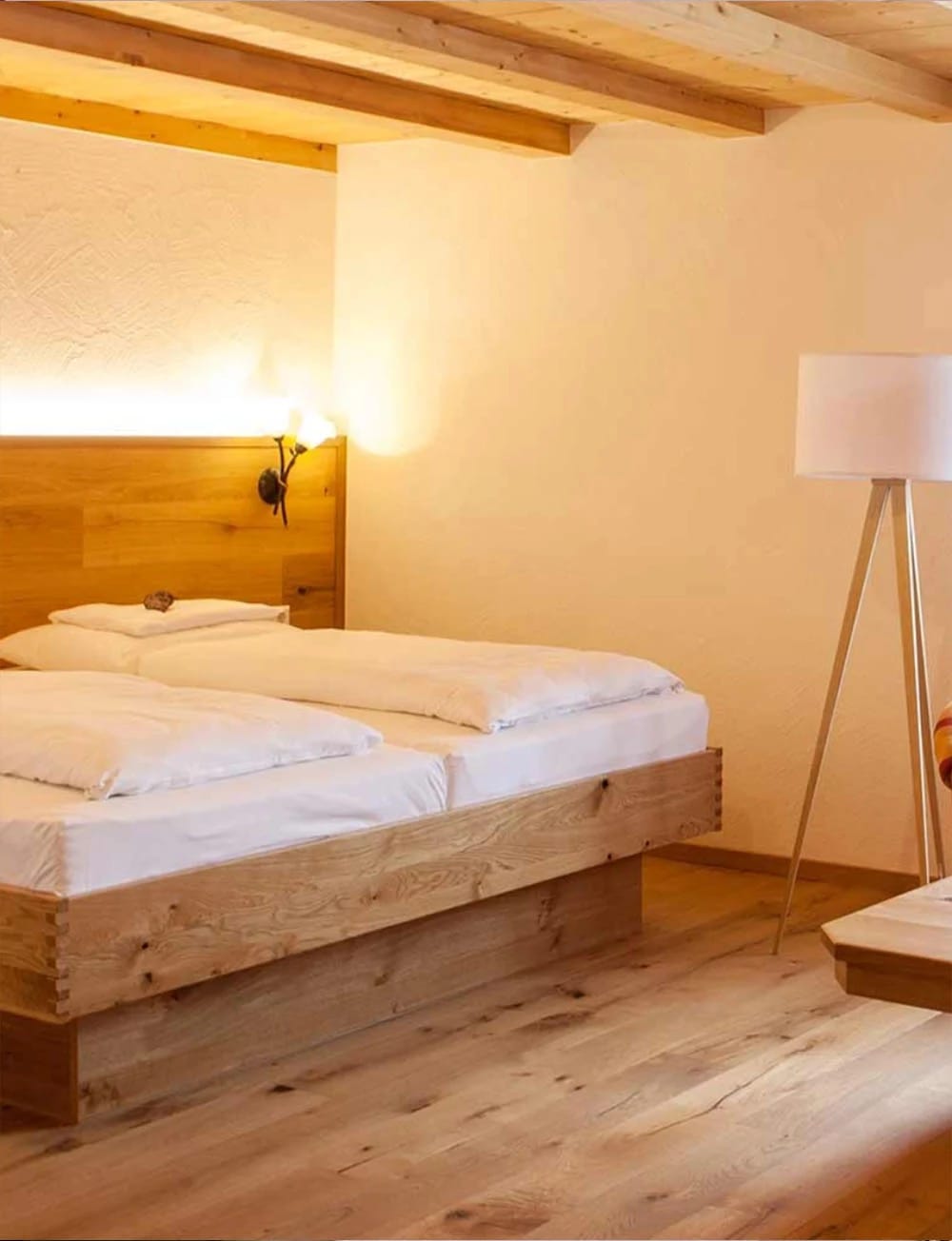 Gemütliches Zimmer mit Holzbett, Stehlampe und sichtbaren Deckenbalken