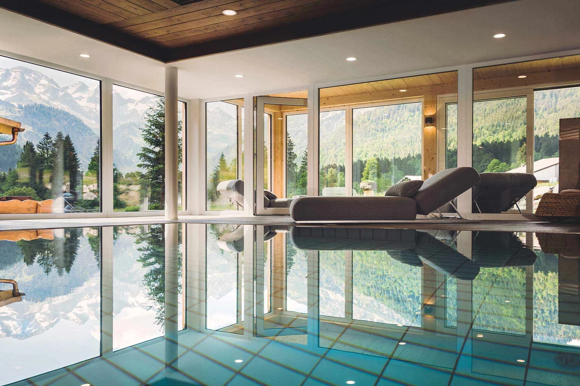 Hallenbad mit bodentiefen Panoramafenstern, Bergblick und Liegen am Beckenrand