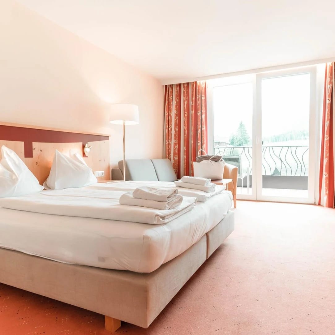 Helles Hotelzimmer mit Doppelbett und Balkon mit Bergblick