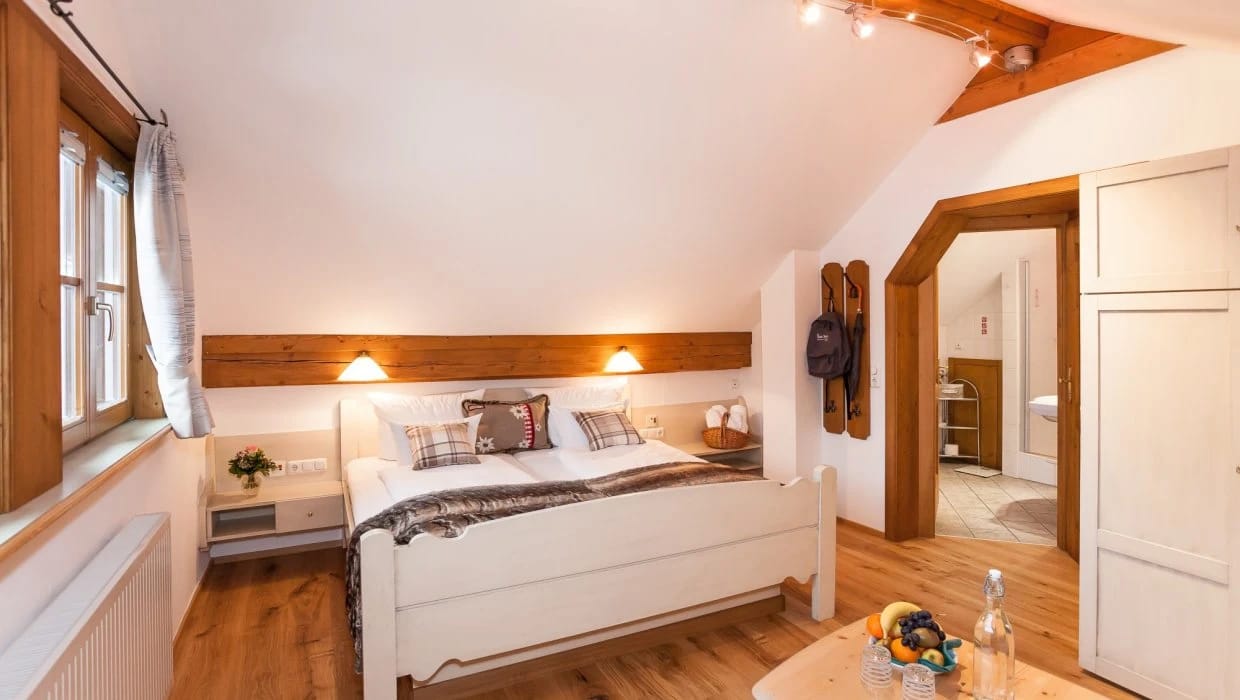 Zimmer mit weißem Holzbett, Fenster und Tür zum Bad