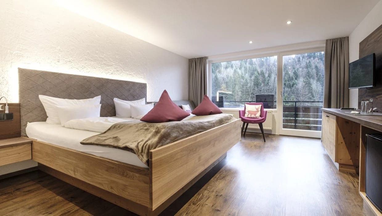 Doppelzimmer mit Holzbett und Balkon mit Blick in den Bergwald