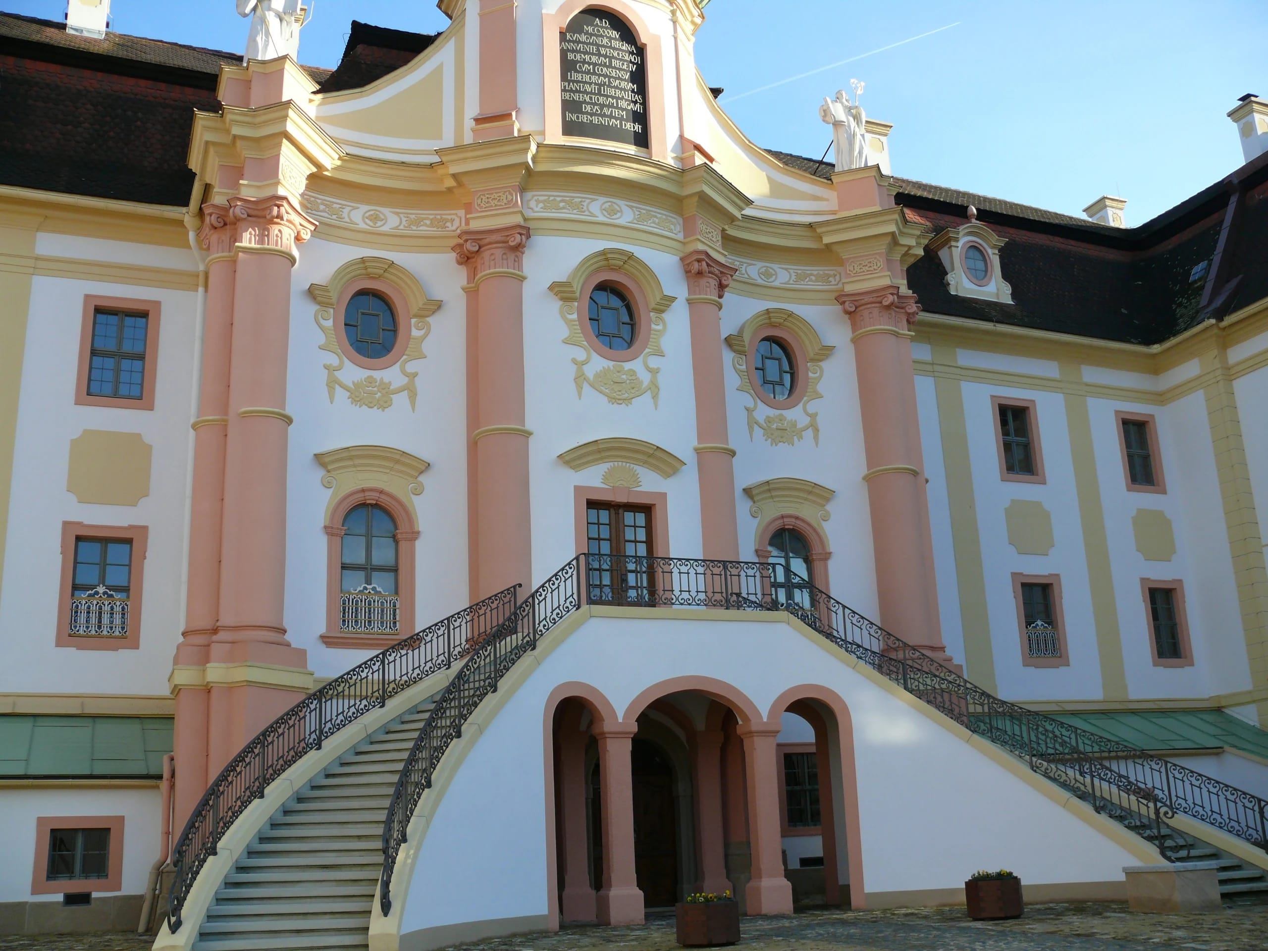 Geschwungene Freitreppe vor der rosa-weißen Barockfassade unter blauem Himmel