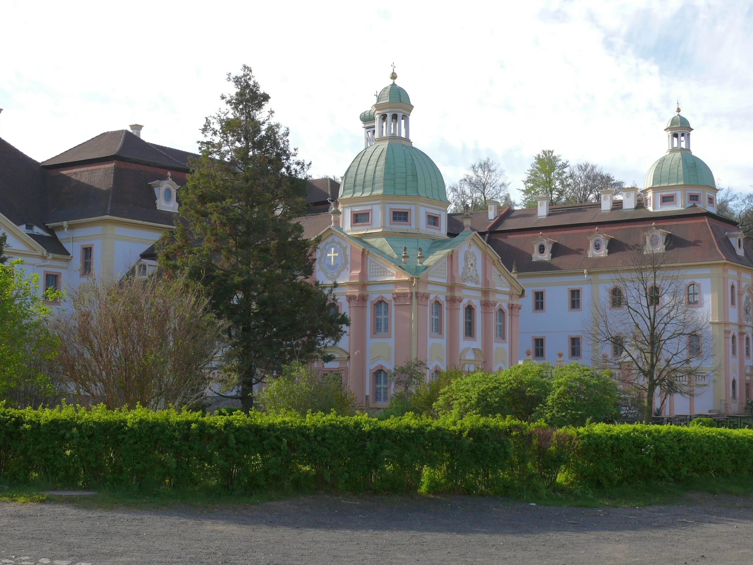 Barocke Klosteranlage mit grün gedeckten Kuppeln hinter Rasenfläche und Hecke