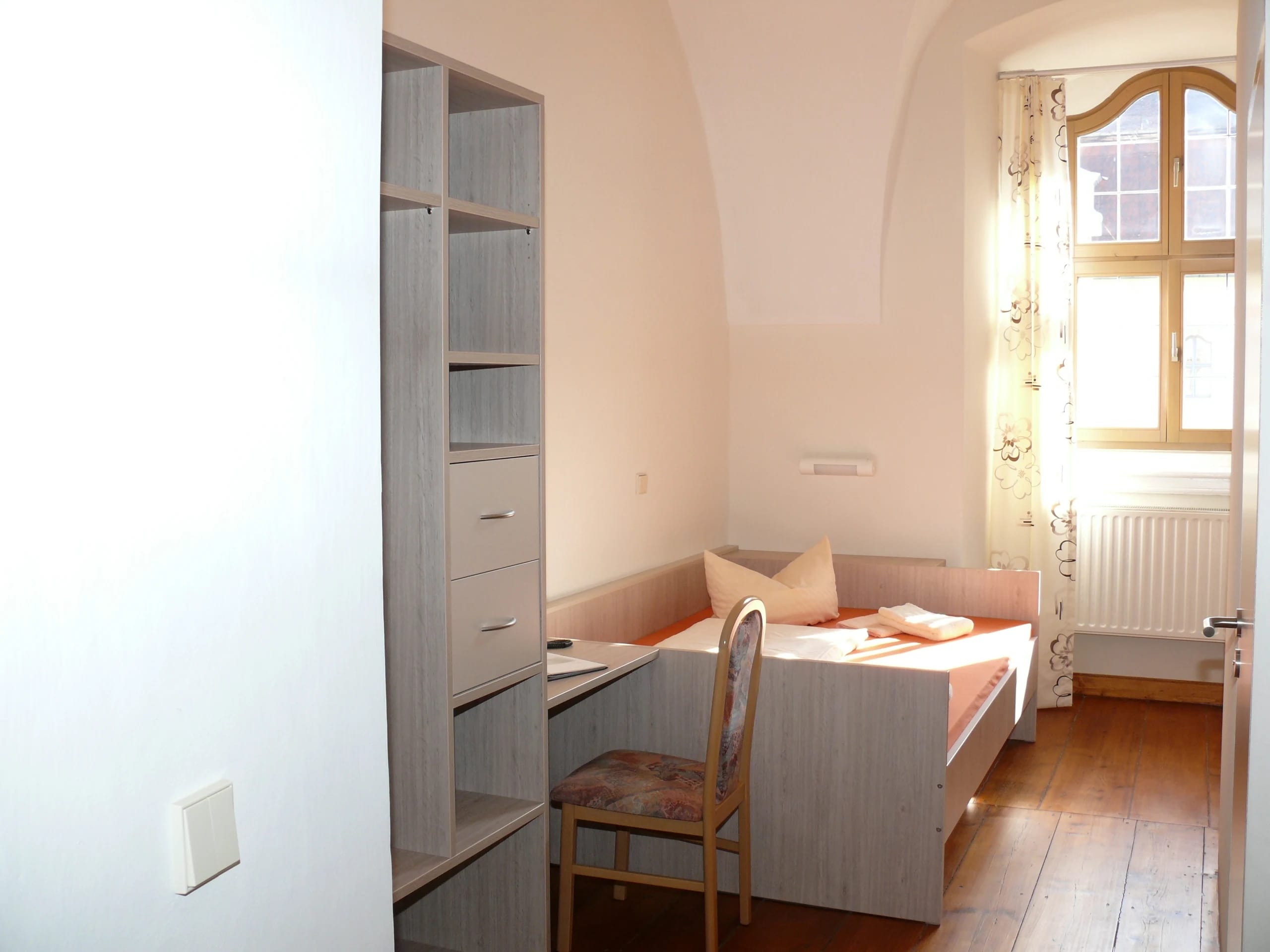 Schlichtes Gästezimmer mit Einzelbett, Schreibtisch und Sprossenfenster unter Gewölbedecke