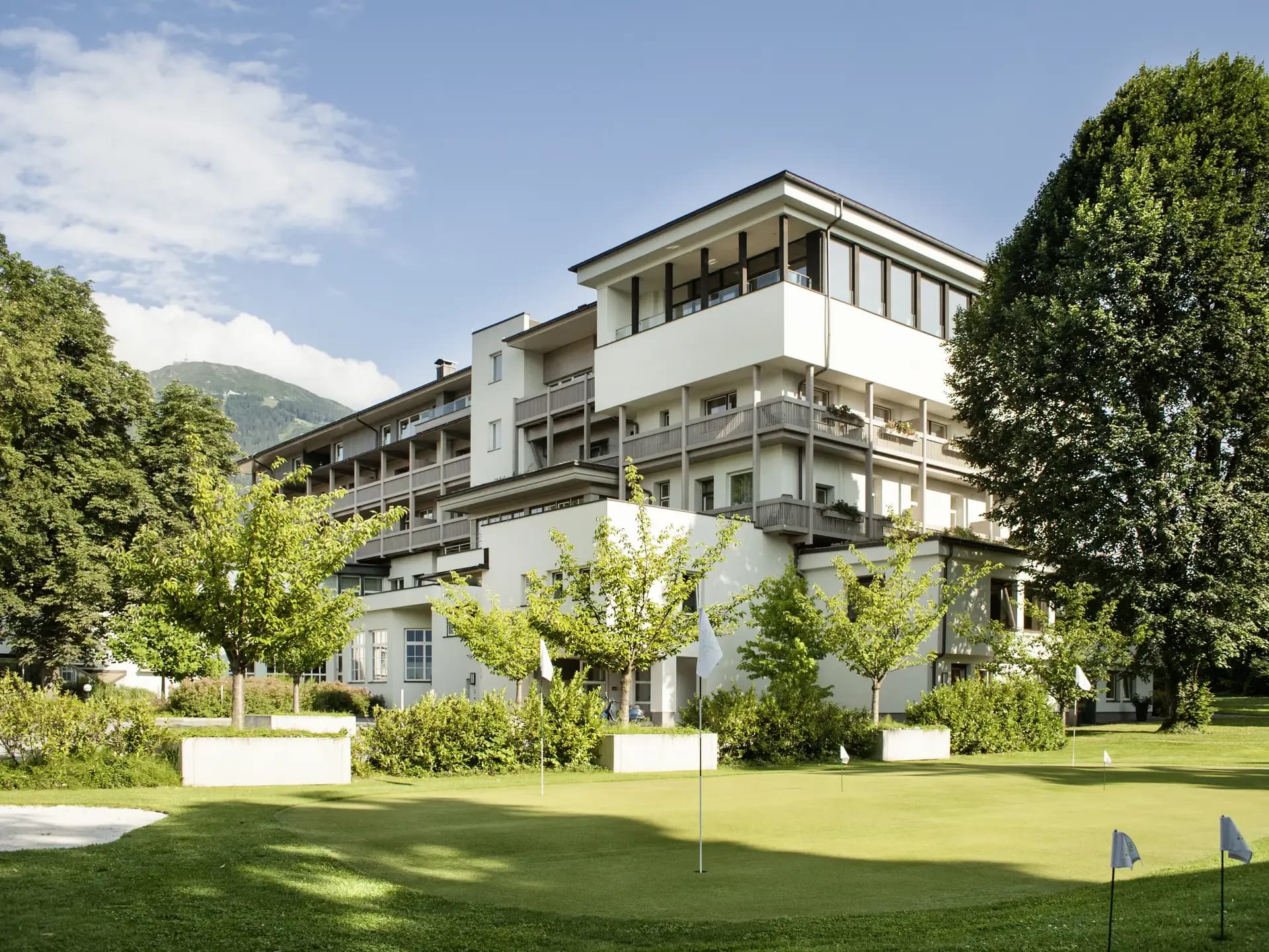 Außenansicht des mehrstöckigen Hotelgebäudes mit Balkonen, davor eine große Rasenfläche mit einzelnen Bäumen