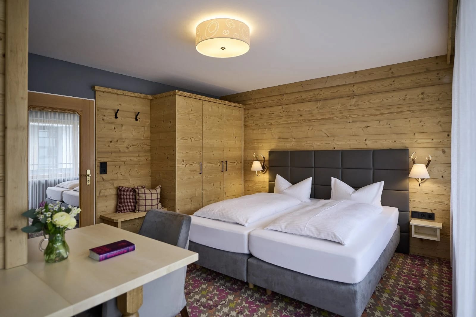 Chalet-Zimmer mit Holzvertäfelung, Doppelbett, Schrank und Tisch mit Stühlen