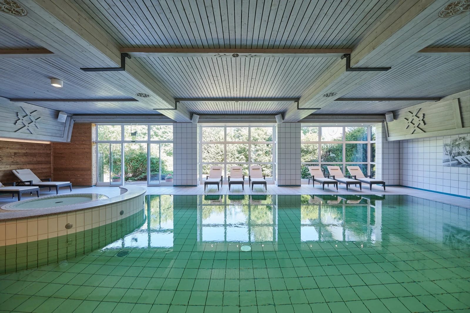 Hallenbad mit grün gefliestem Becken, Whirlpool und Liegen an der Fensterfront
