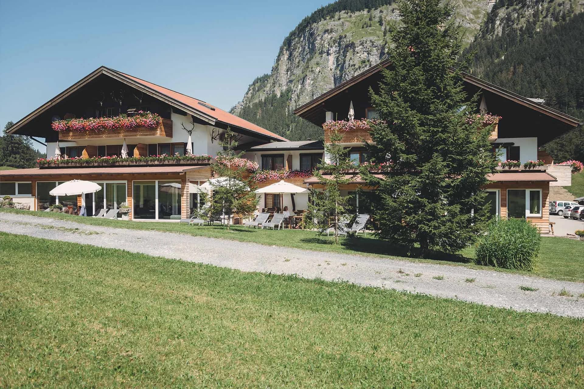 Hausfassade mit Balkonen und Blumenkästen, davor eine Terrasse mit Sonnenschirmen und Liegestühlen