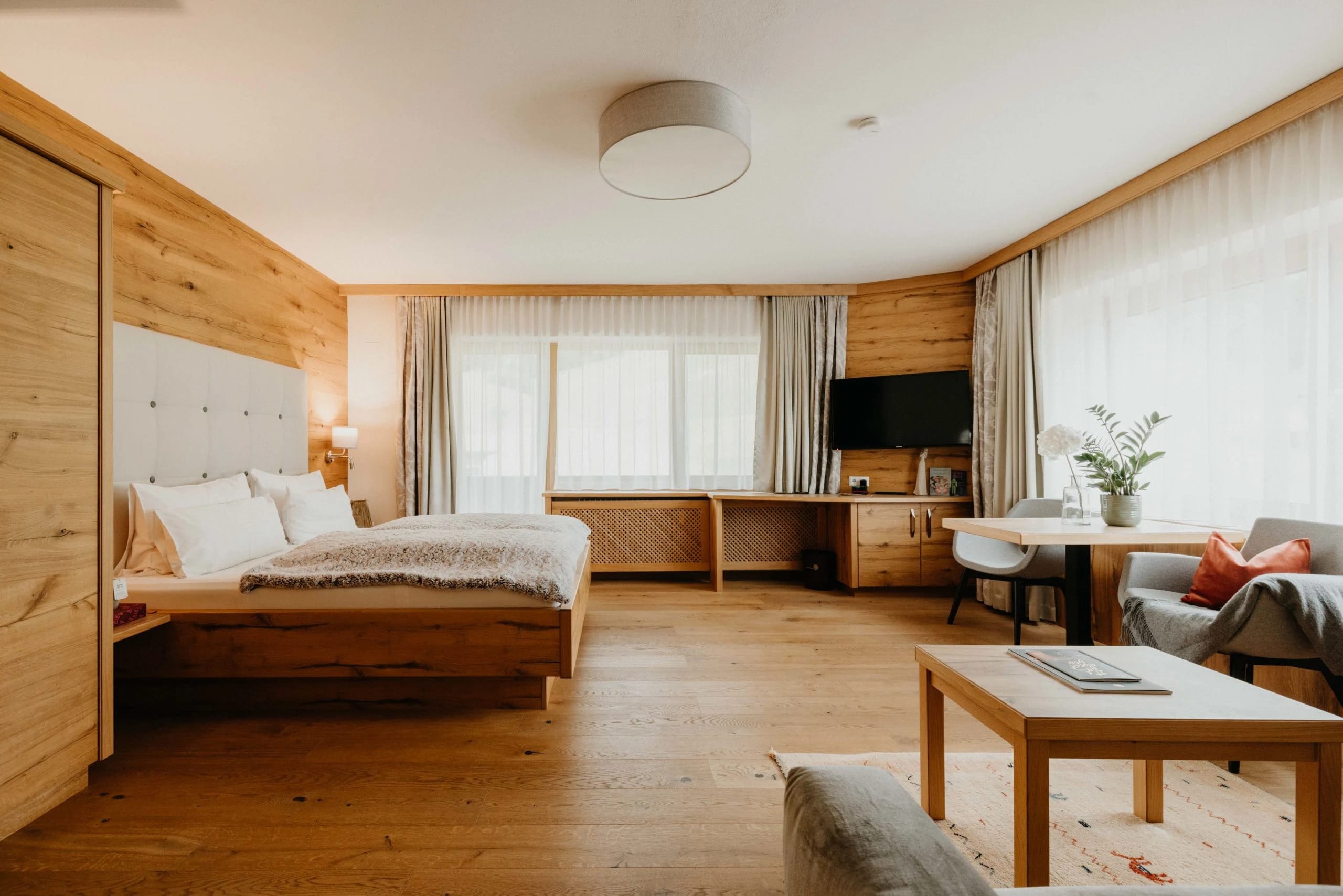 Helles Zimmer mit Holzwand, Doppelbett, Schreibtisch und Sitzecke
