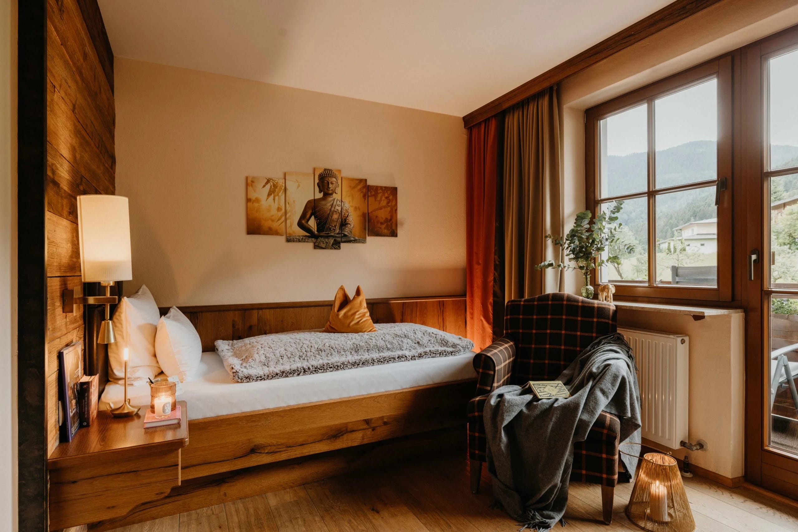 Zimmer mit Holzbett, Sessel und Fenster mit Blick auf bewaldete Hügel