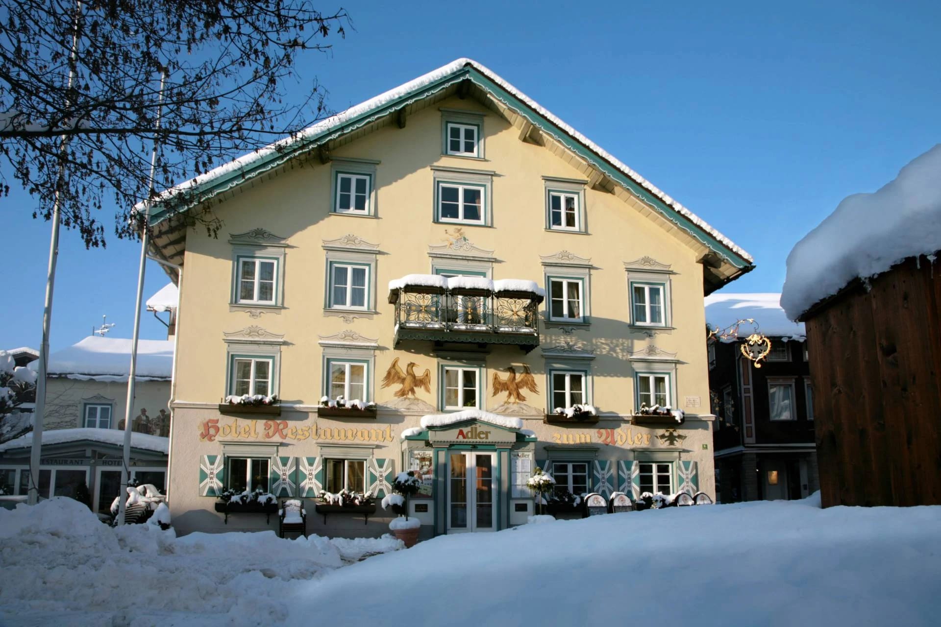 Verschneite Außenansicht des Hotelgebäudes mit schmiedeeisernem Balkon vor blauem Winterhimmel