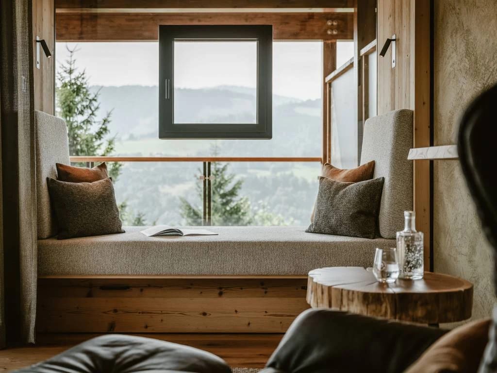 Gepolsterte Fensterbank mit Kissen und Blick auf bewaldete Hügel