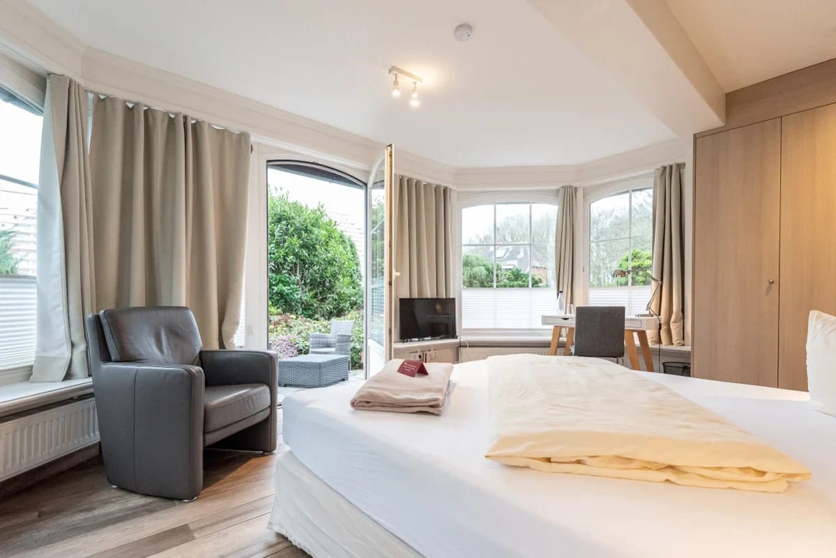 Helles Zimmer mit Doppelbett, Ledersessel und Erkerfenster mit Blick in den Garten