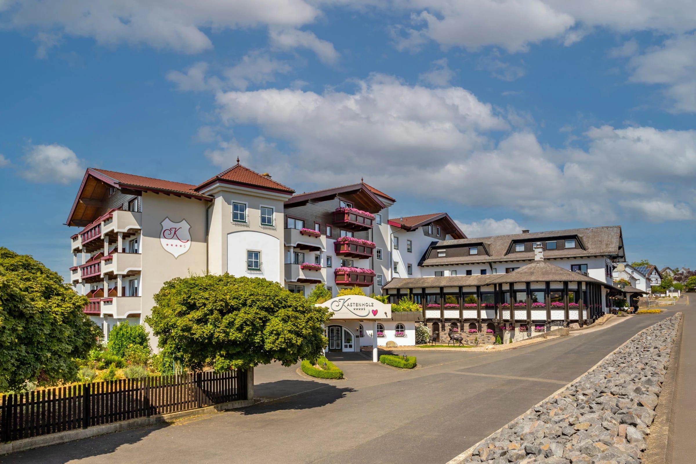Straßenansicht des Hotels mit rot-weißen Balkonen und angrenzendem Fachwerkhaus