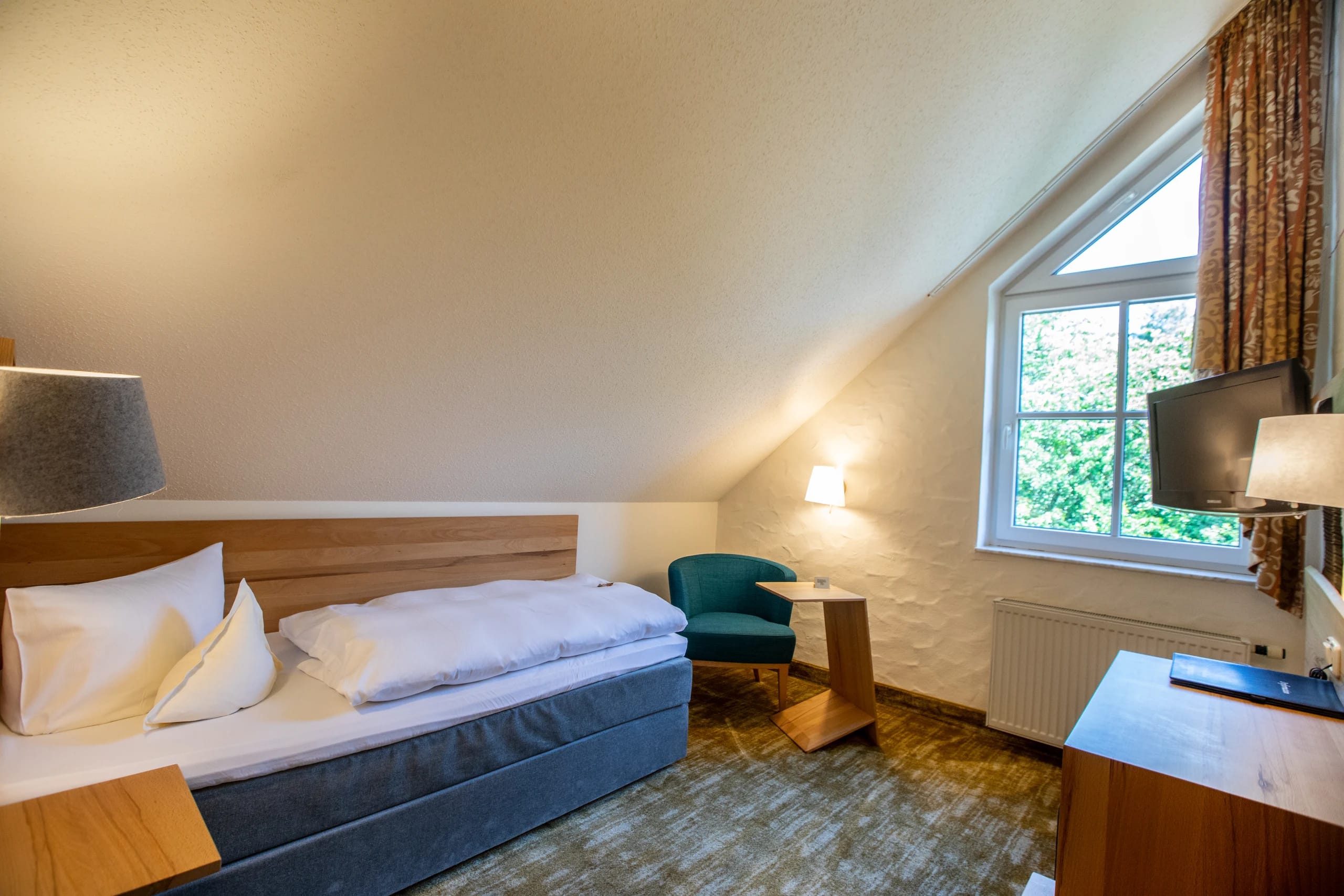 Einzelzimmer mit Bett, Sessel und Fenster unter der Dachschräge