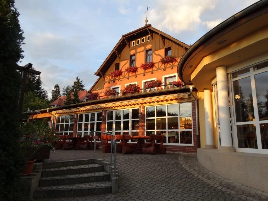 Hauptgebäude mit Fachwerkgiebel, Blumenkästen und Wintergarten, davor die Terrasse mit roten Stühlen im Abendlicht