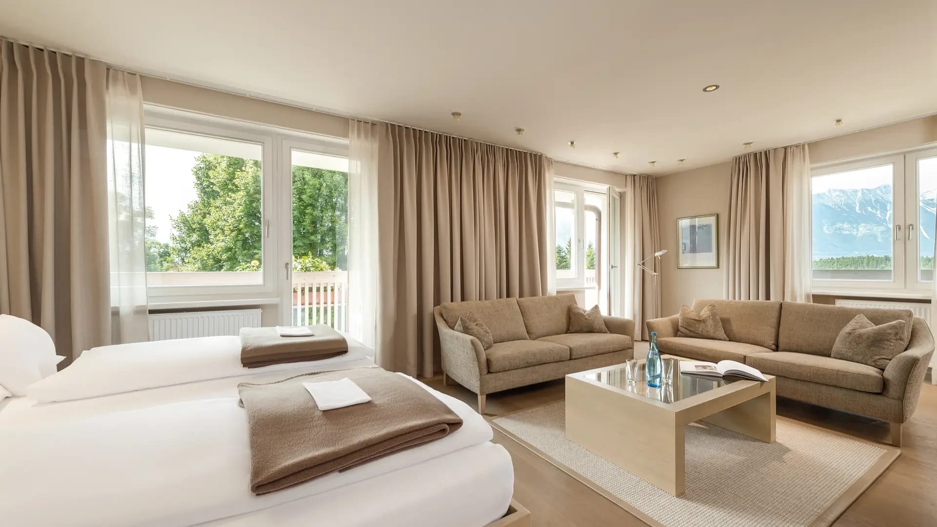 Helles Zimmer mit Doppelbett, zwei Sofas, Couchtisch und großen Fenstern mit Balkontür