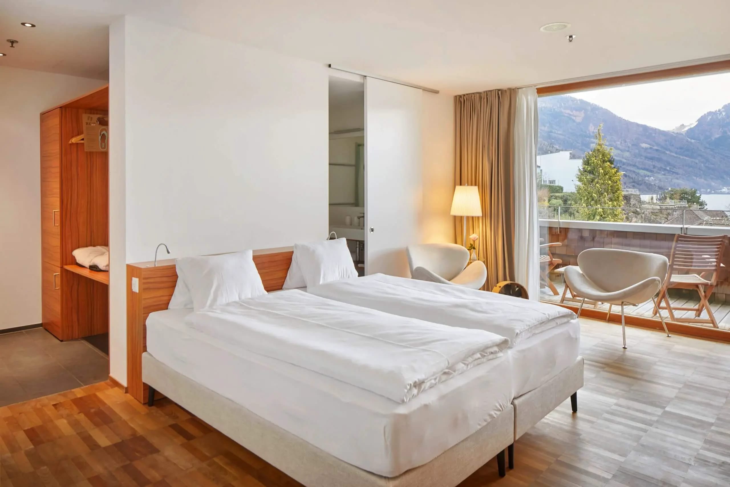 Geräumiges Zimmer mit Doppelbett, Sesselecke und großem Fenster mit Blick auf See und Berge